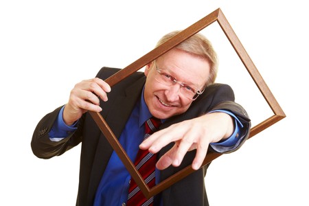 Smiling senior businessman looking through an empty picture frameの写真素材