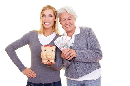 Elderly woman with banknotes looking over to young woman with piggy bankの写真素材