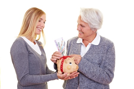 Grandmother putting money in piggy bank of her granddaughterの写真素材