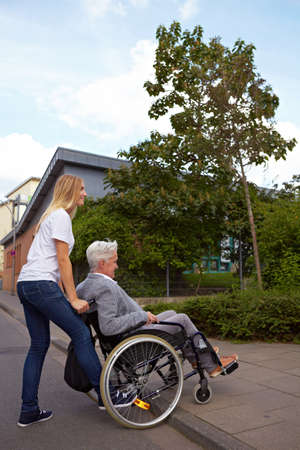 Young woman helping elderly woman in wheelchair over a curbstoneの写真素材