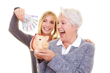 Young and old woman putting money in piggy bank for pensionの写真素材