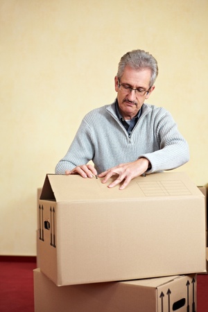 Elderly man opening the lid of a packing case while relocation houseの写真素材