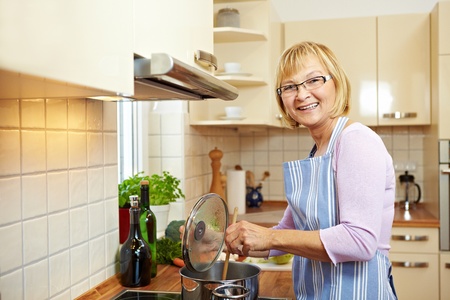 Elderly woman in kitchen on a stove cooking soupの写真素材