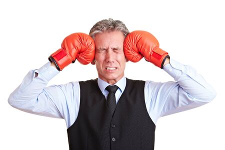 Senior manager pushing red boxing gloves against his aching headの写真素材