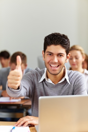 Successful student at laptop holding his thumbs upの写真素材