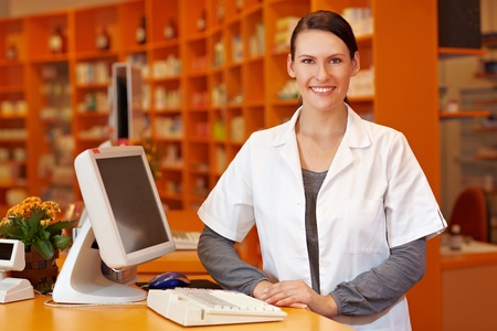 Happy pharmacist standing at checkout counter in a drugstoreの写真素材