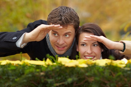 Happy couple looking over a hedge in autumnの写真素材