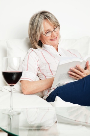 Relaxed senior woman reading a book with glass of wineの写真素材