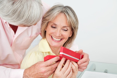 Happy smiling senior woman receiving gift from her husbandの写真素材