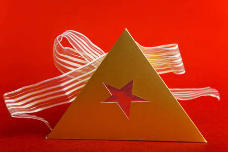 Christmas gift with pyramide shape and bow on red backgroundの写真素材