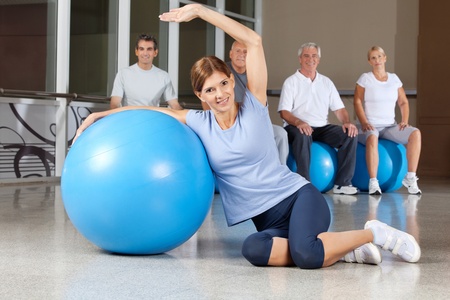 Happy woman doing back exercises with blue gym ball in fitness centerの写真素材