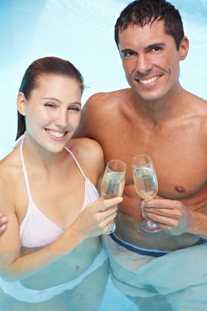 Happy smiling couple in swimming pool drinking sparkling wineの写真素材