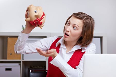 Shocked woman in office shaking a piggy bankの写真素材