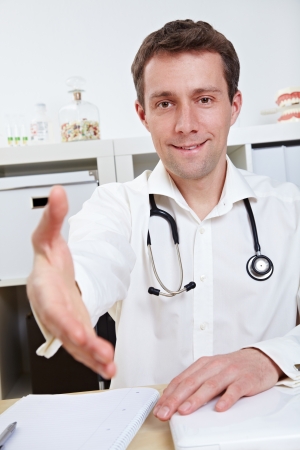 Physician at his desk offering hand for handshake in his officeの写真素材