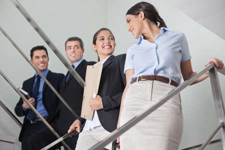 Smiling businessmen flirting with two attractive women in the office stairwayの写真素材