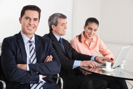 Smiling manager with his arms crossed sitting in the office with team in backgroundの写真素材