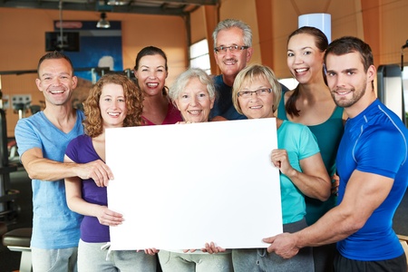 Big happy group holding empty white poster in fitness centerの写真素材