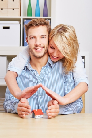 Happy couple holding their hands protectivly over a small houseの写真素材