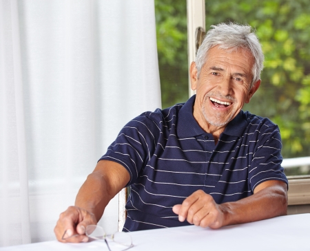 Happy smiling senior man sitting with reading glasses at a tableの写真素材