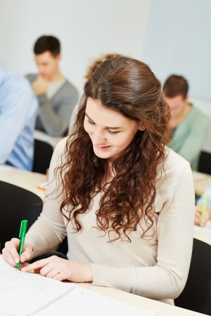 Happy female student taking notes in university course classroomの写真素材