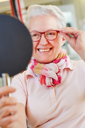 Nearsighted senior woman with new glasses looking into mirror at opticianの写真素材