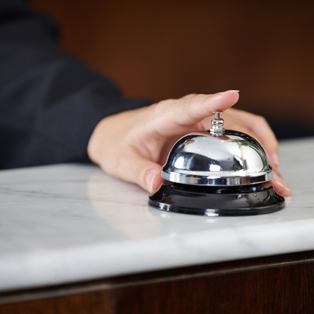 Female hand ringing hotel bell at the counter with index fingerの写真素材