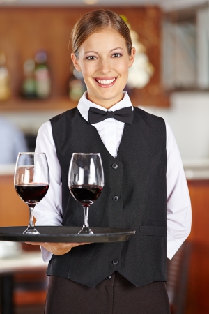 Happy female waiter with two red wine glasses in a restaurantの写真素材