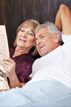 Two senior people reading newspaper together in a bedの写真素材