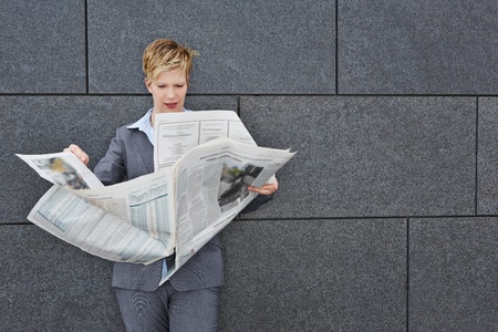 Business woman reading a daily newspaper in windy weather outdoorsの写真素材