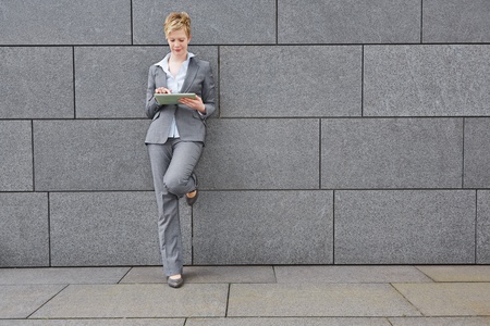 Business woman with tablet computer in the city leaning on a wallの写真素材