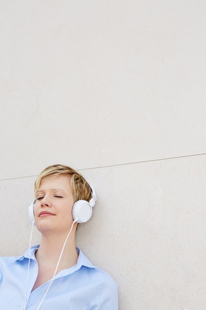 Young relaxed woman leaning on wall listening to music with headphonesの写真素材