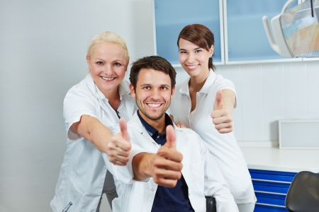 Happy dentist and smiling dental team holding their thumbs up in dental practiceの写真素材