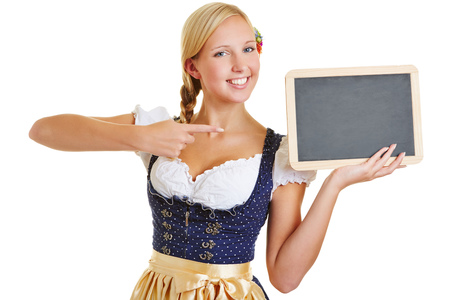 Happy young woman in a dirndl pointing with her index finger to empty blackboardの写真素材