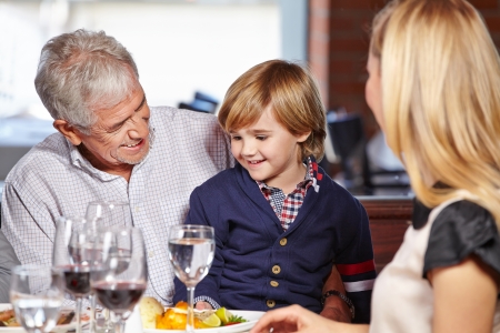Family with smiling grandfather and his grandchild eating out in a restaurantの写真素材