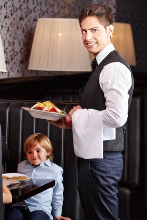 Happy waiter serving salad food in a restaurantの写真素材