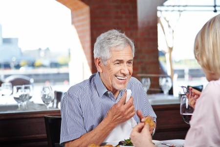Happy elderly man cleaning his mouth with napkin at a restaurantの写真素材