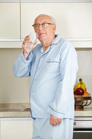 Senior man in his pajamas drinking a glass of water in the kitchenの写真素材