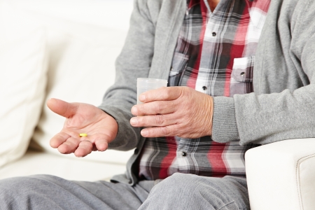 Old man taking medical pills with a cup of waterの写真素材