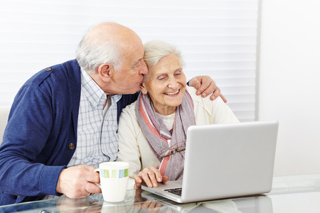 Man kissing happy senior woman at the computer on the cheek