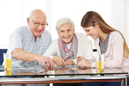 Couple senior citizens playing with a jigsaw puzzle with her granddaughterの写真素材