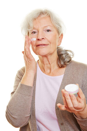Elderly senior woman putting skin care lotion on her faceの写真素材