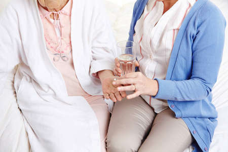 Senior citizen woman getting pill with water from a nurseの写真素材