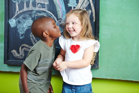 African boy kissing happy girl on the cheek in a kindergartenの写真素材
