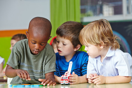 Three children in kindergarten playing with building blocks and carsの写真素材