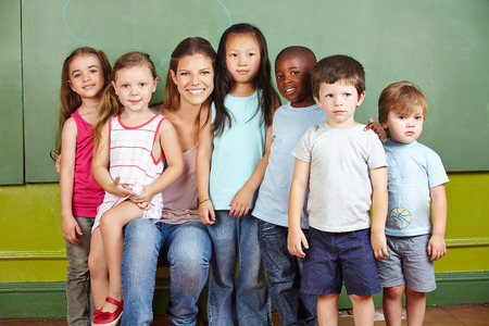 Happy group of children with smiling kindergarten teacher in a roomの写真素材