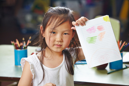 Asian girl showing her drawing in a kindergartenの写真素材