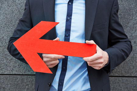 Business man holding big red arrow to the leftの写真素材
