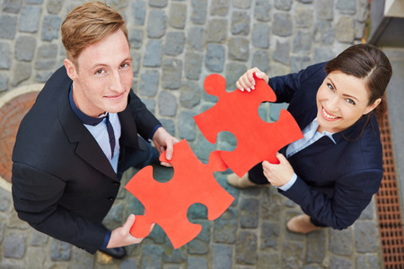Smiling man and happy woman holding big red jigsaw puzzle piecesの写真素材
