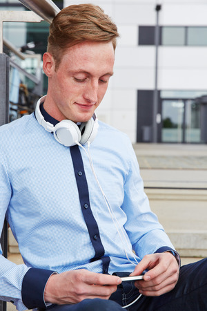 Young man with headphones and smartphone sitting in the cityの写真素材