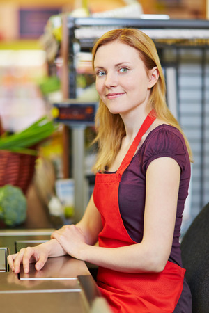 Young smiling cashier sitting at supermarket checkoutの写真素材